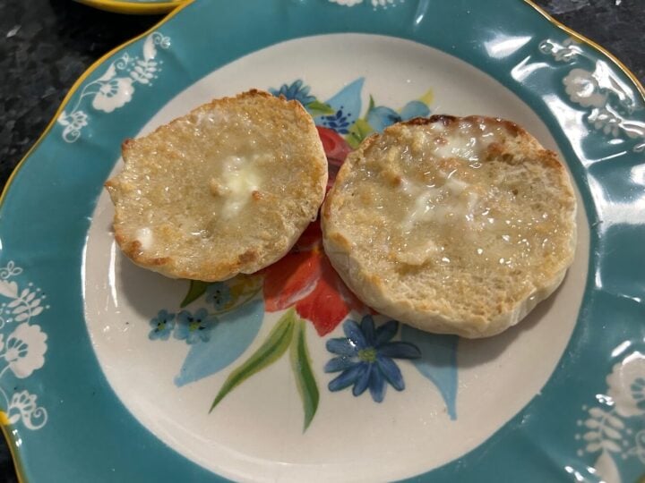 Homemade sourdough English muffins split open and toasted with melting butter on a floral plate.