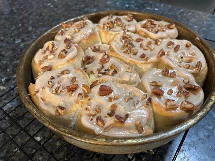 pumpkin spice cinnamon rolls in pan, iced with pecans