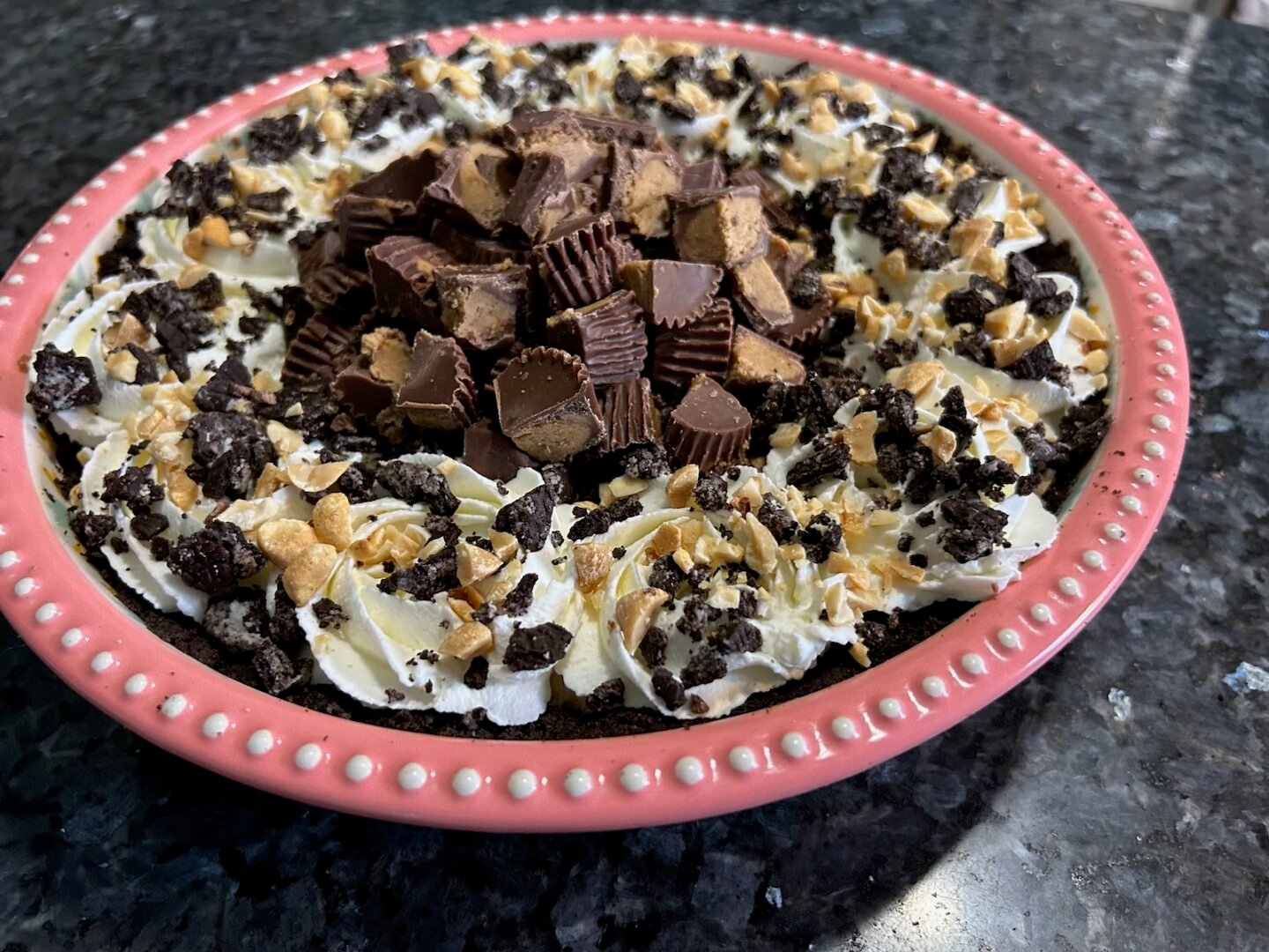 peanut butter pie, fully decorated with whipped cream, Reese's peanut butter cups, and peanuts