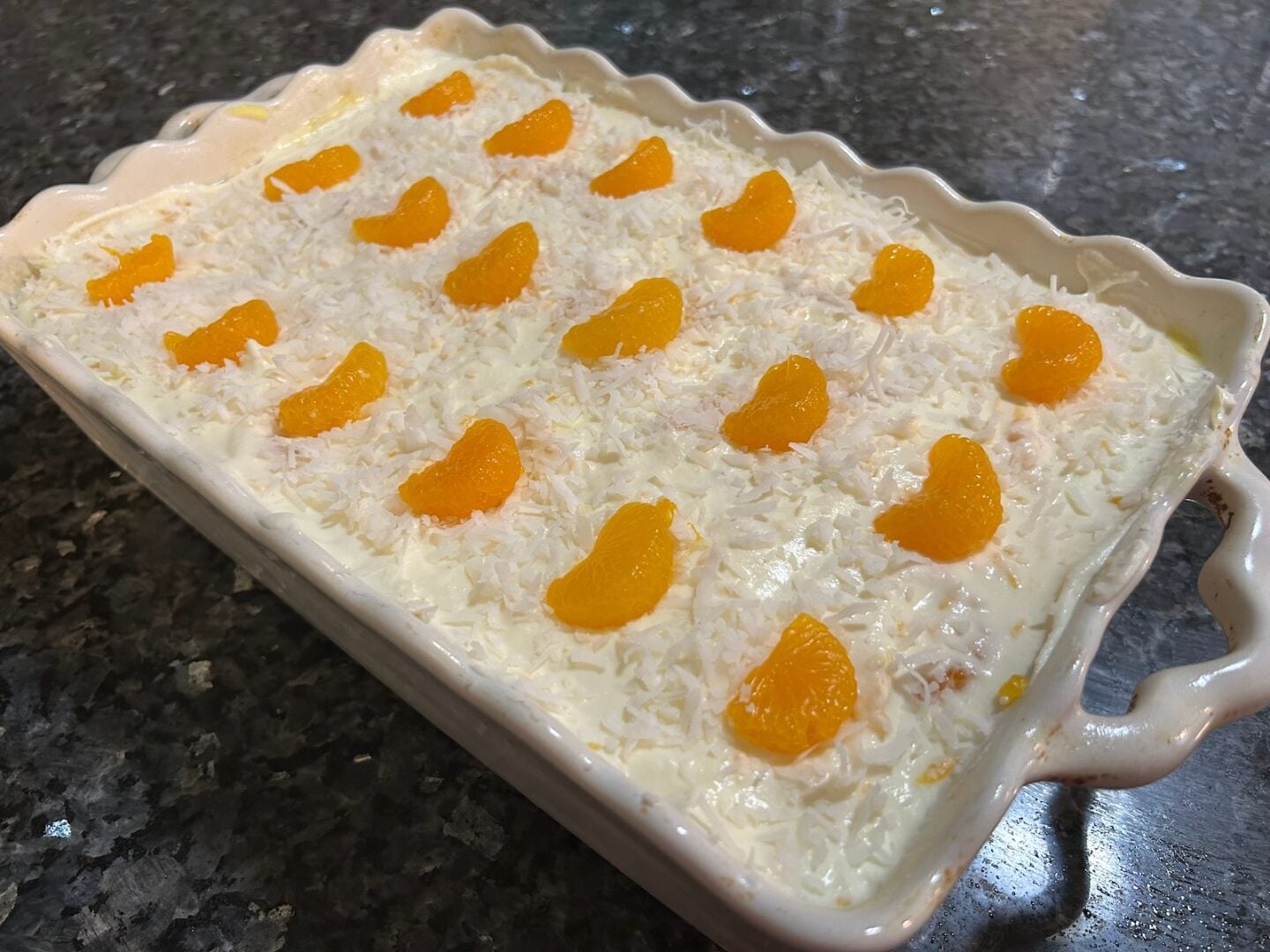 whole mandarin orange poke cake in pan, decorated with mandarin orange slices