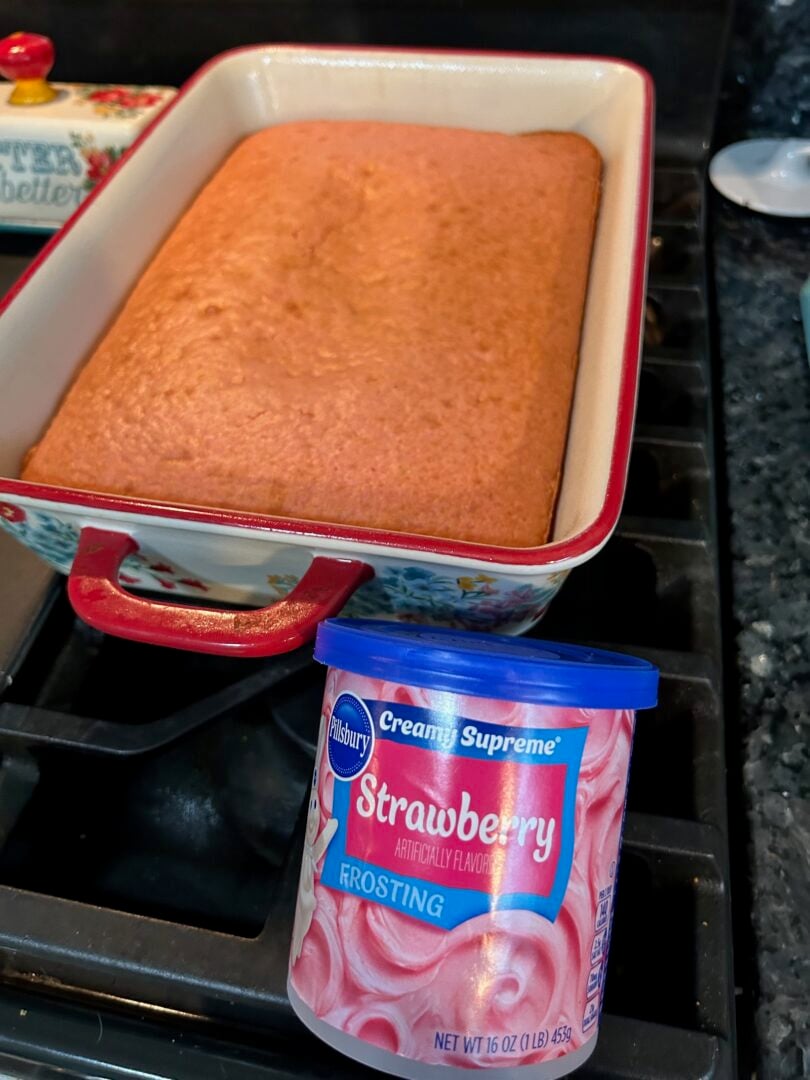 baked strawberry cake in pan with frosting nearby