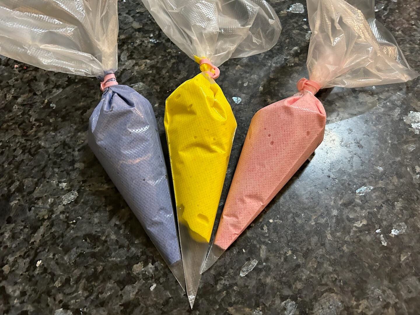 macaron batter in piping bags: pink, yellow, lavender