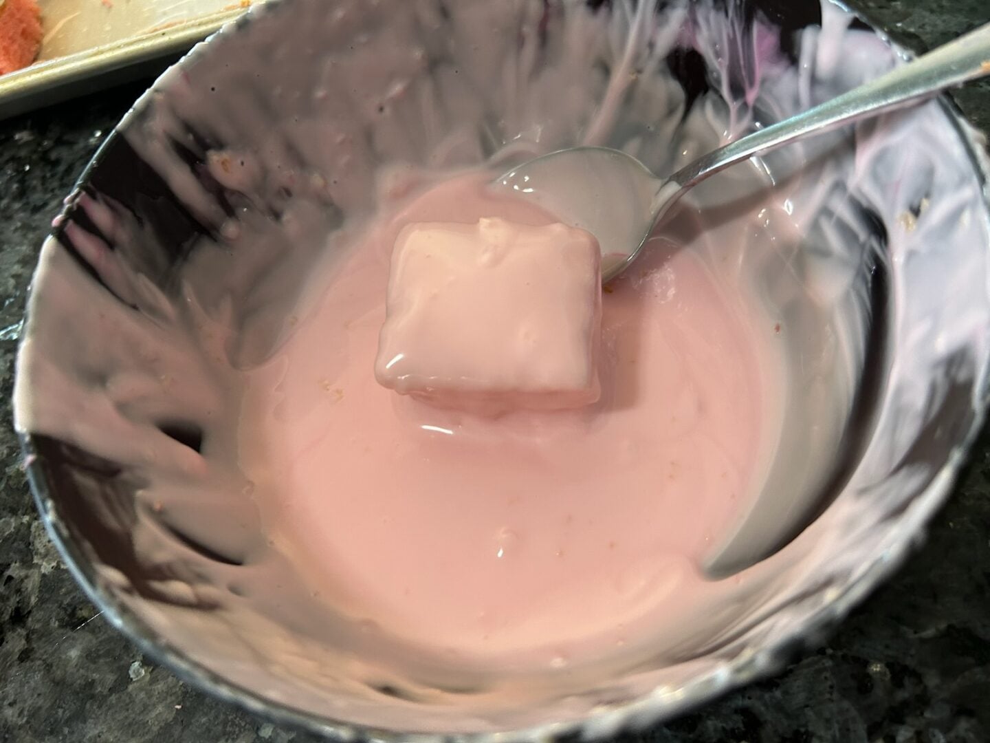 dipping petit four in bowl of melted almond bark