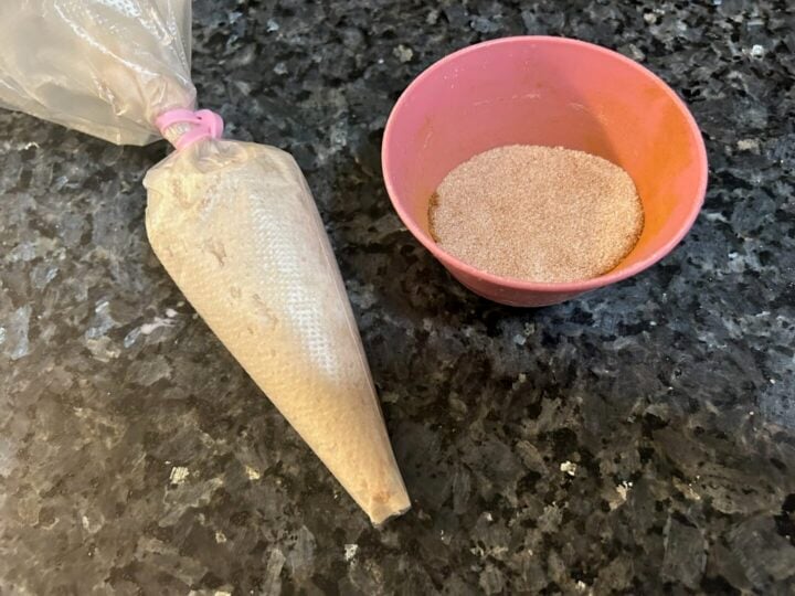 buttercream in piping bag next to bowl of cinnamon sugar mixture