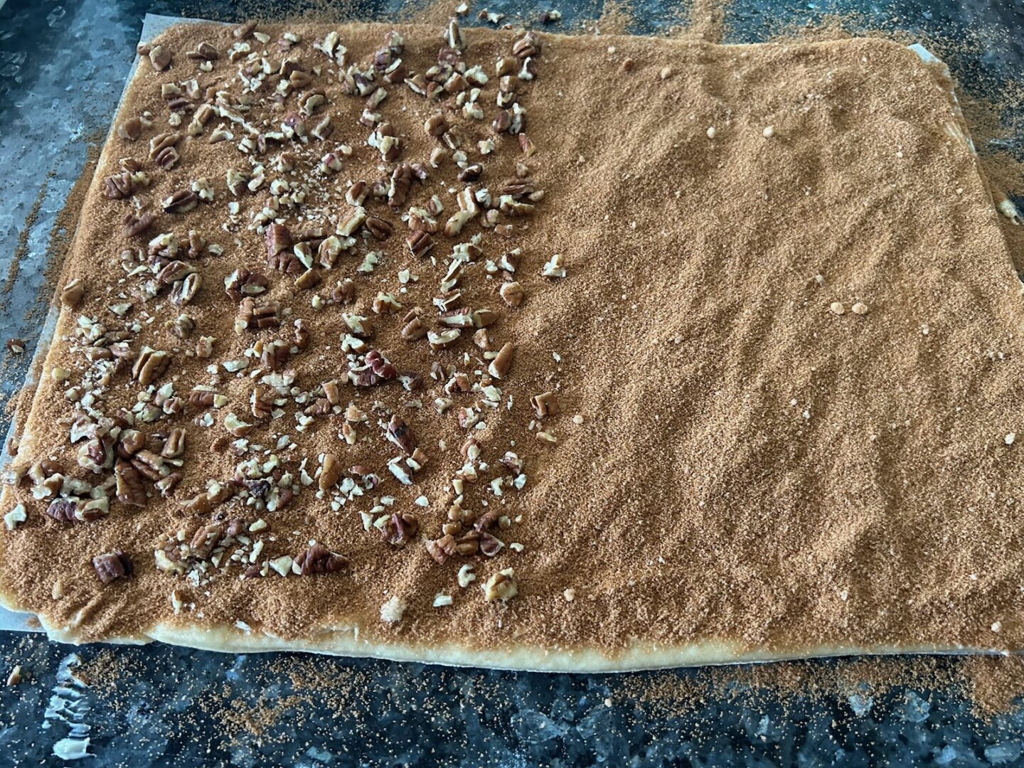 cinnamon roll dough with cinnamon and brown sugar on top along with chopped pecans on half