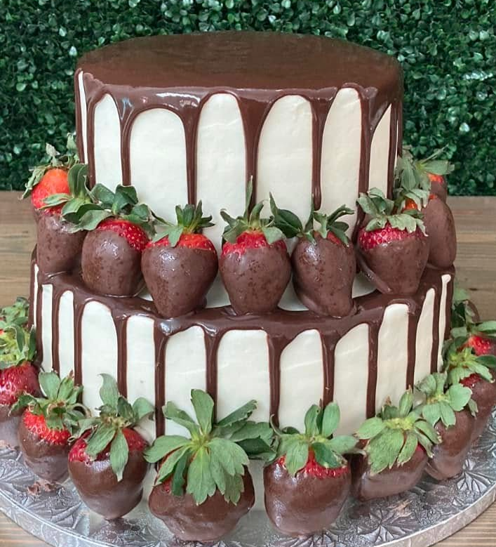 gorgeous two-tiered groom's cake with white frosting, ganache drip, and chocolate covered strawberries