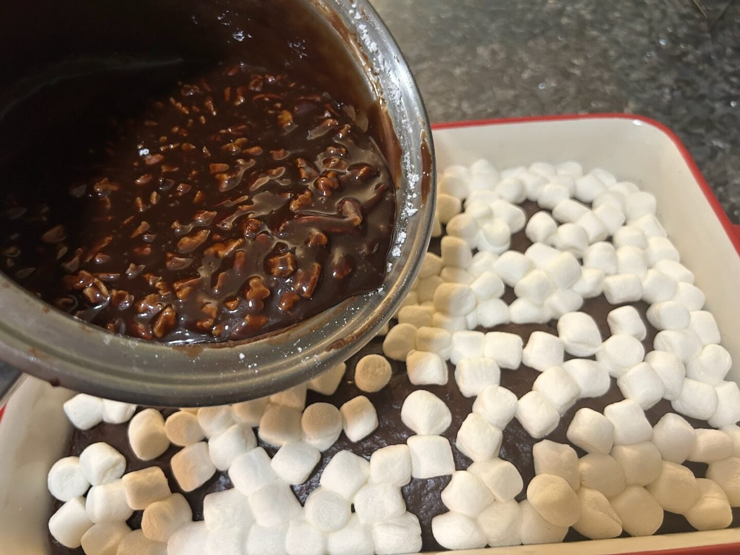 chocolate cake with marshmallows on top and chocolate frosting being added
