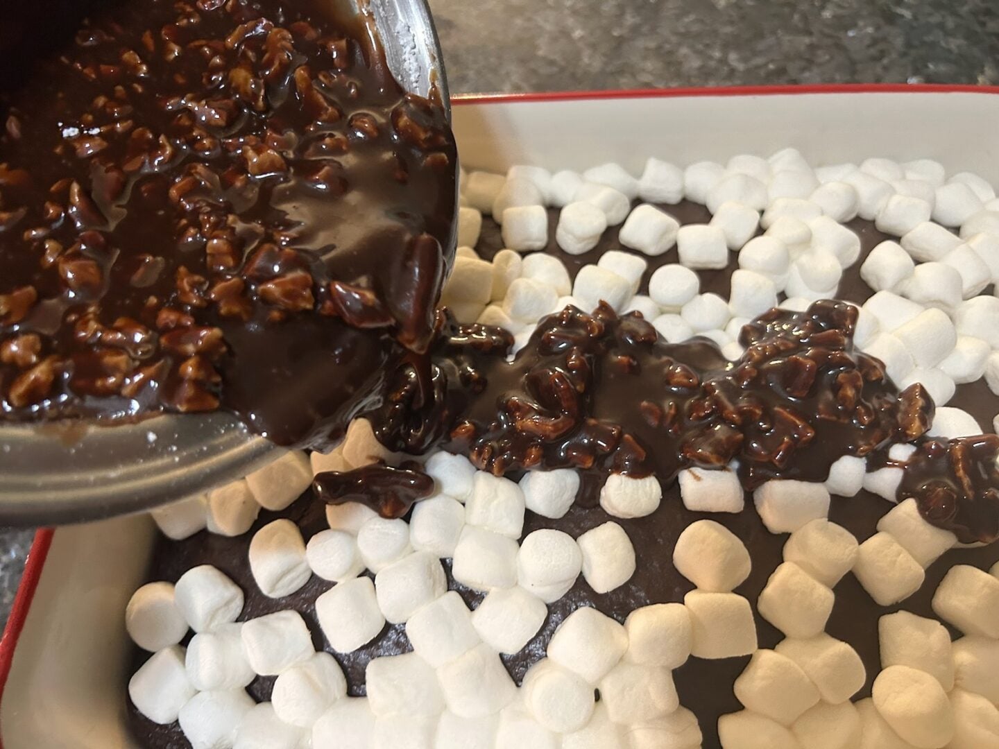 chocolate cake with marshmallows on top and chocolate frosting being added
