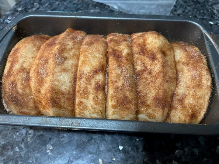covering bread dough risen and covered in butter and cinnamon sugar, ready to bake
