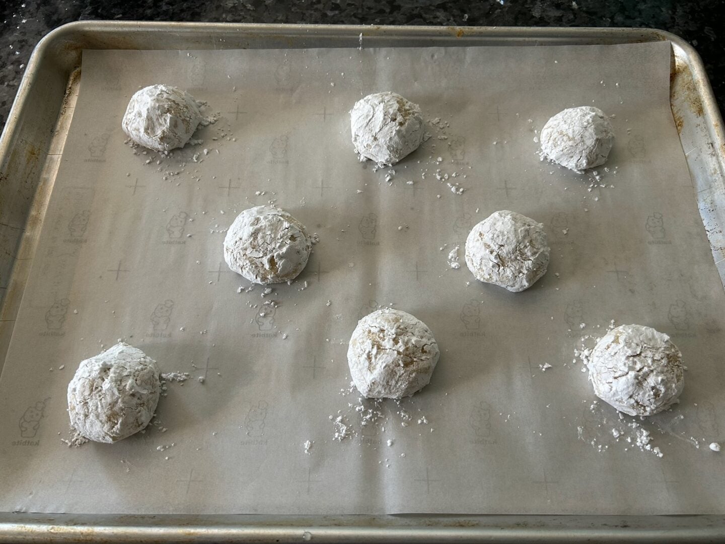 cookie dough balls rolled in powdered sugar and placed on cookie sheet